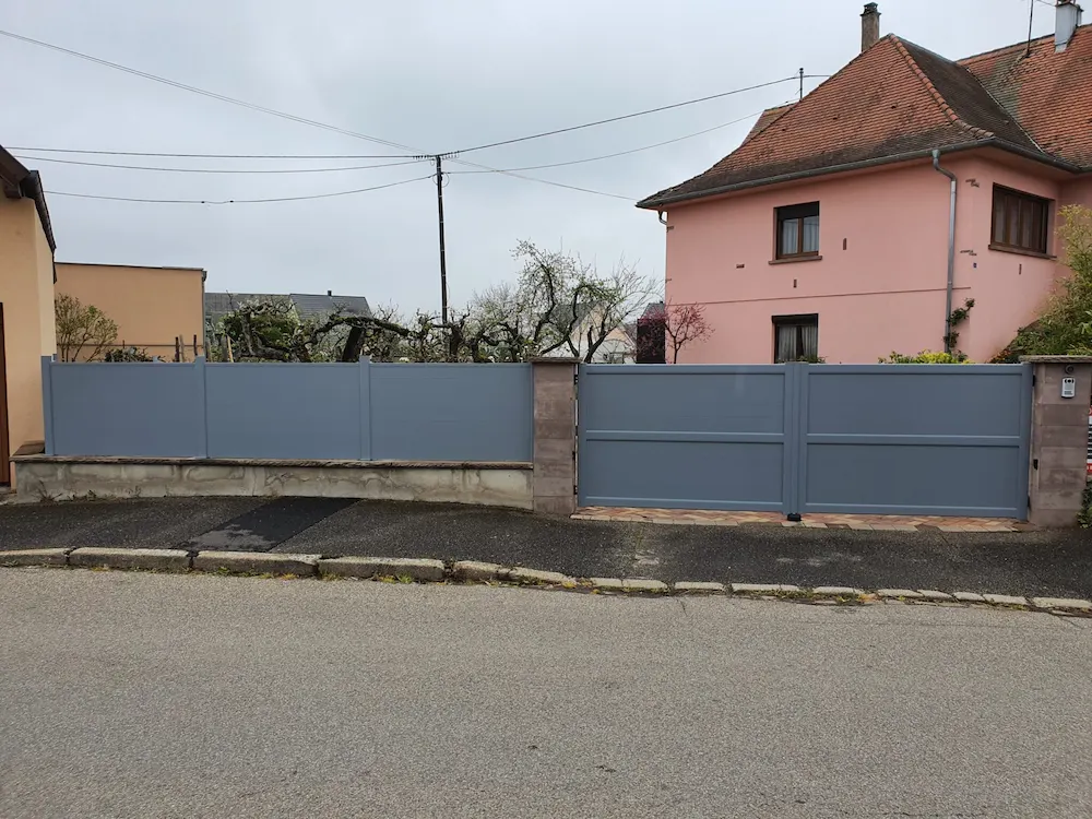 Installation d'un portail 2 battants plein en aluminium gris clair avec panneaux brise-vue assortis pour une occultation totale de la propriété.