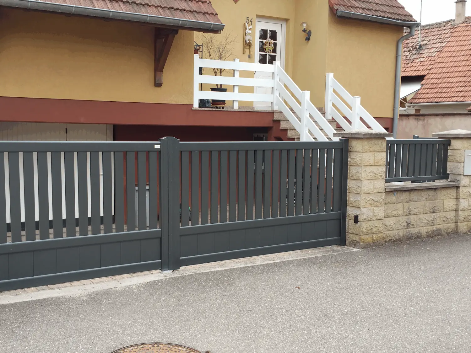 Portail battant motorisé gris anthracite avec lames verticales ajourées et soubassement plein assorti à la clôture à Sermersheim.