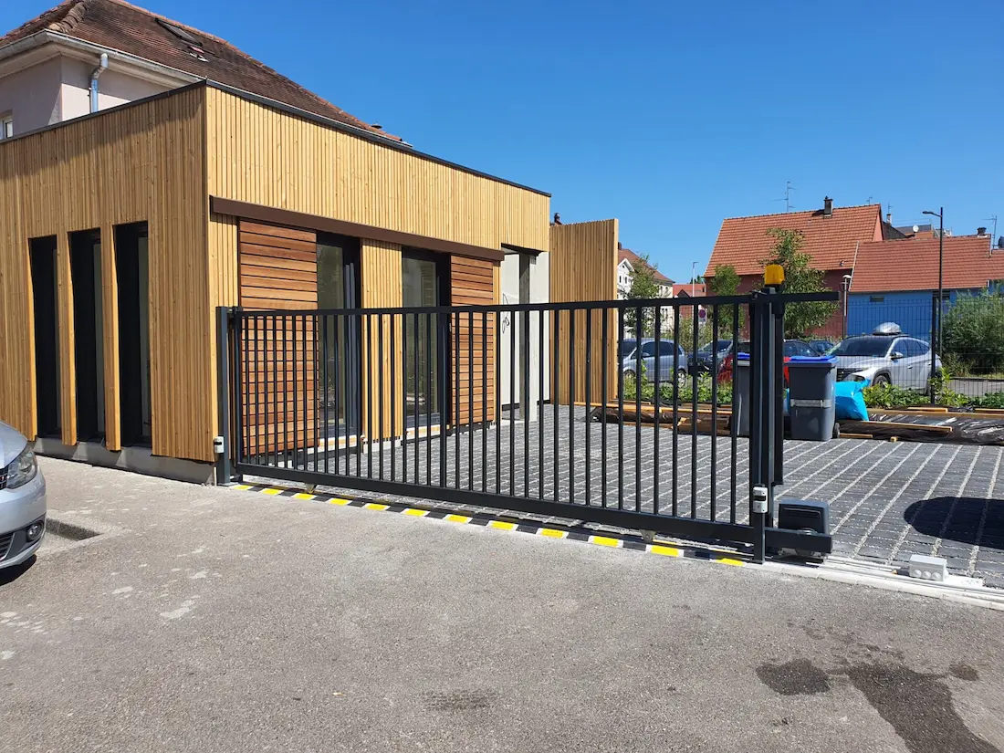 Portail coulissant motorisé noir style industriel à barreaux fins avec marquage de sécurité au sol à Plobsheim.