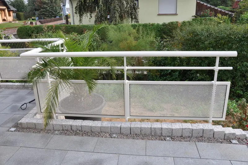 Vue depuis le jardin d'un garde-corps en aluminium blanc avec remplissage en tôle perforée, offrant un design léger et une protection visuelle pour une terrasse à Westhouse.